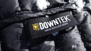 Close-up of a black down jacket with water droplets and snow on it, showing a DownTek Water Repellent Down label.